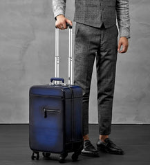 View of model grabbing the extended telescopic handle of the blue-colored rolling bag. The rolling is positioned at 45° angle with both the front and one side of the case being shown 